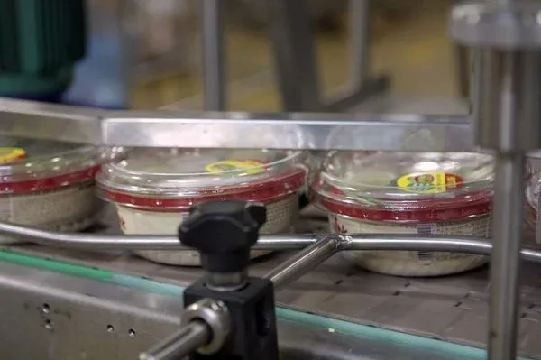 Finished sealed hummus cups on conveyor belt ready for distribution